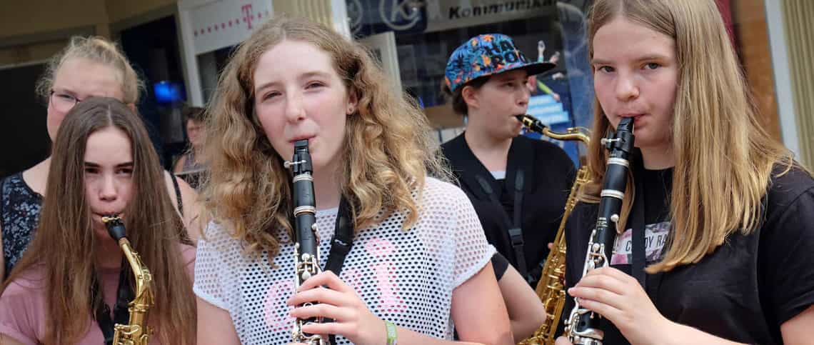 Vier Teilnehmerinnen des EMMA MädchenMusikcamps. Die Teilnehmerinnen rechts spielen lächelnd Klarinette, die Teilnehmerinnen links neben ihr und im Hintergrund jeweils Saxofon.